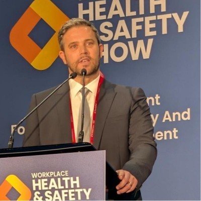 Man in a suit speaking at a podium during a health and safety show.