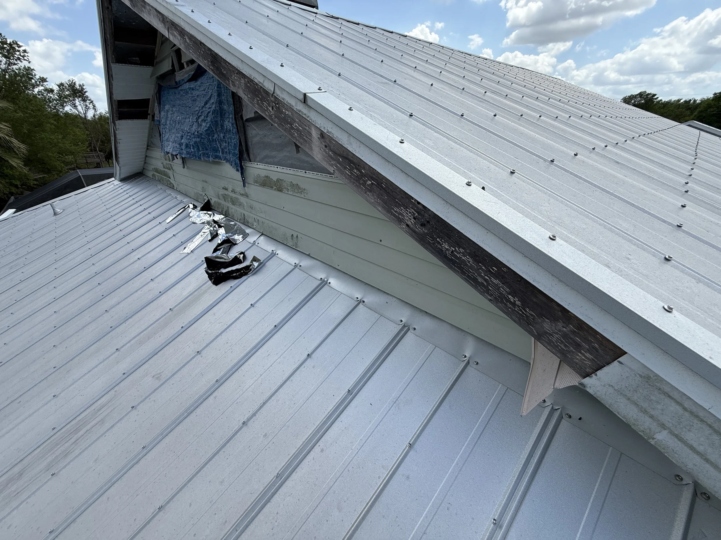 Torn soffit and flashing damage on a metal roof after storm exposure