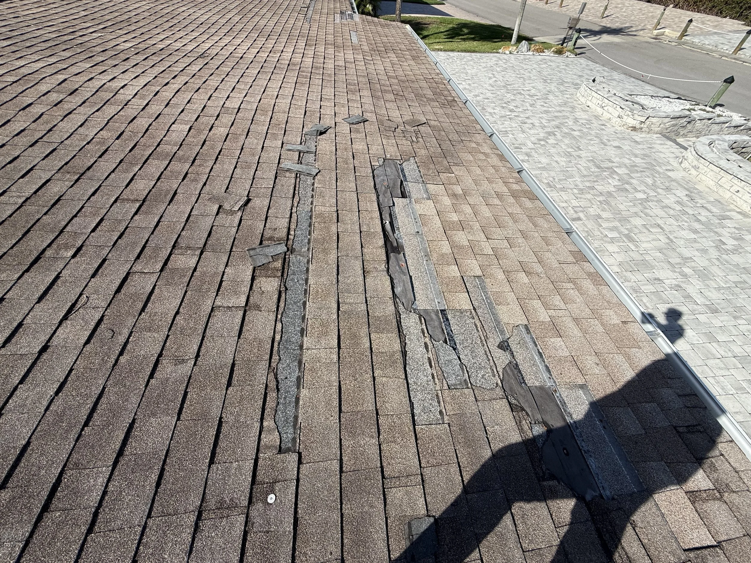 Wind-damaged asphalt shingle roof showing prior patch repairs