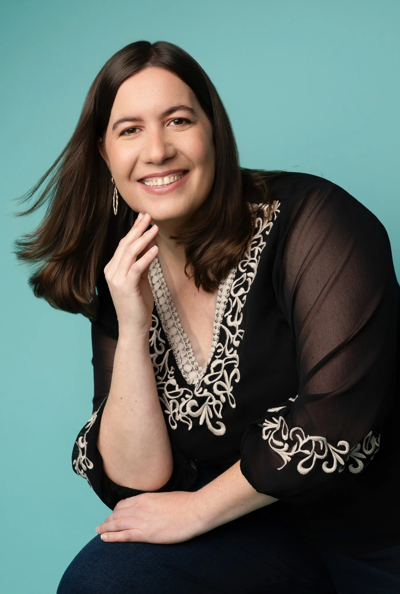 Bright Professional Portrait of Woman in Embroidered Black Top on Teal Background