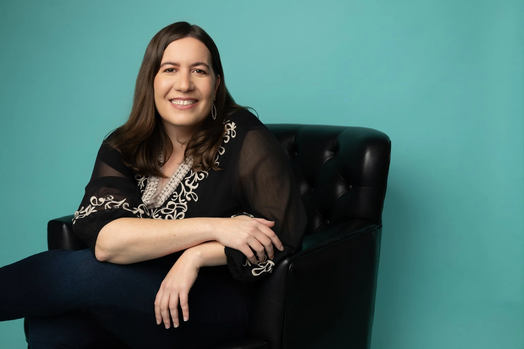 Relaxed Branding Portrait of Woman Seated on Black Chair With Teal Background