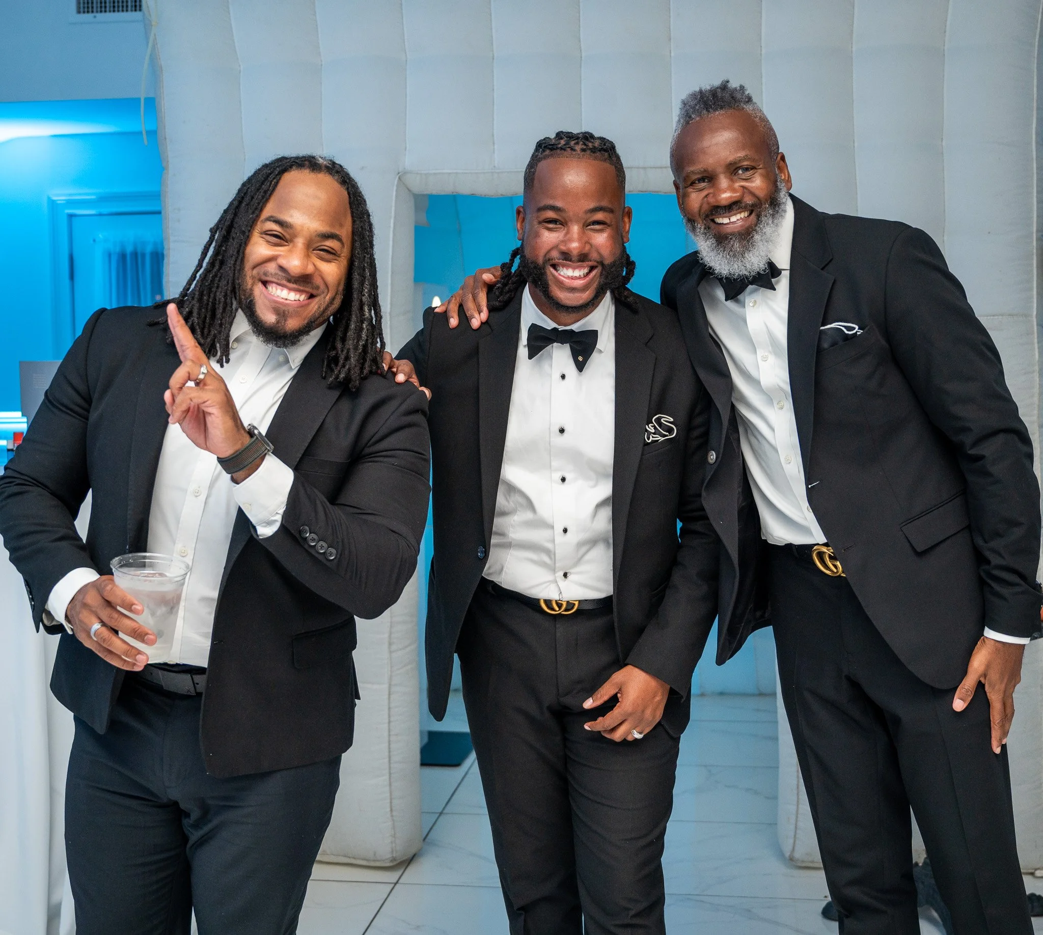 three African American men dressed in tuxedos, smiling at a formal event.
