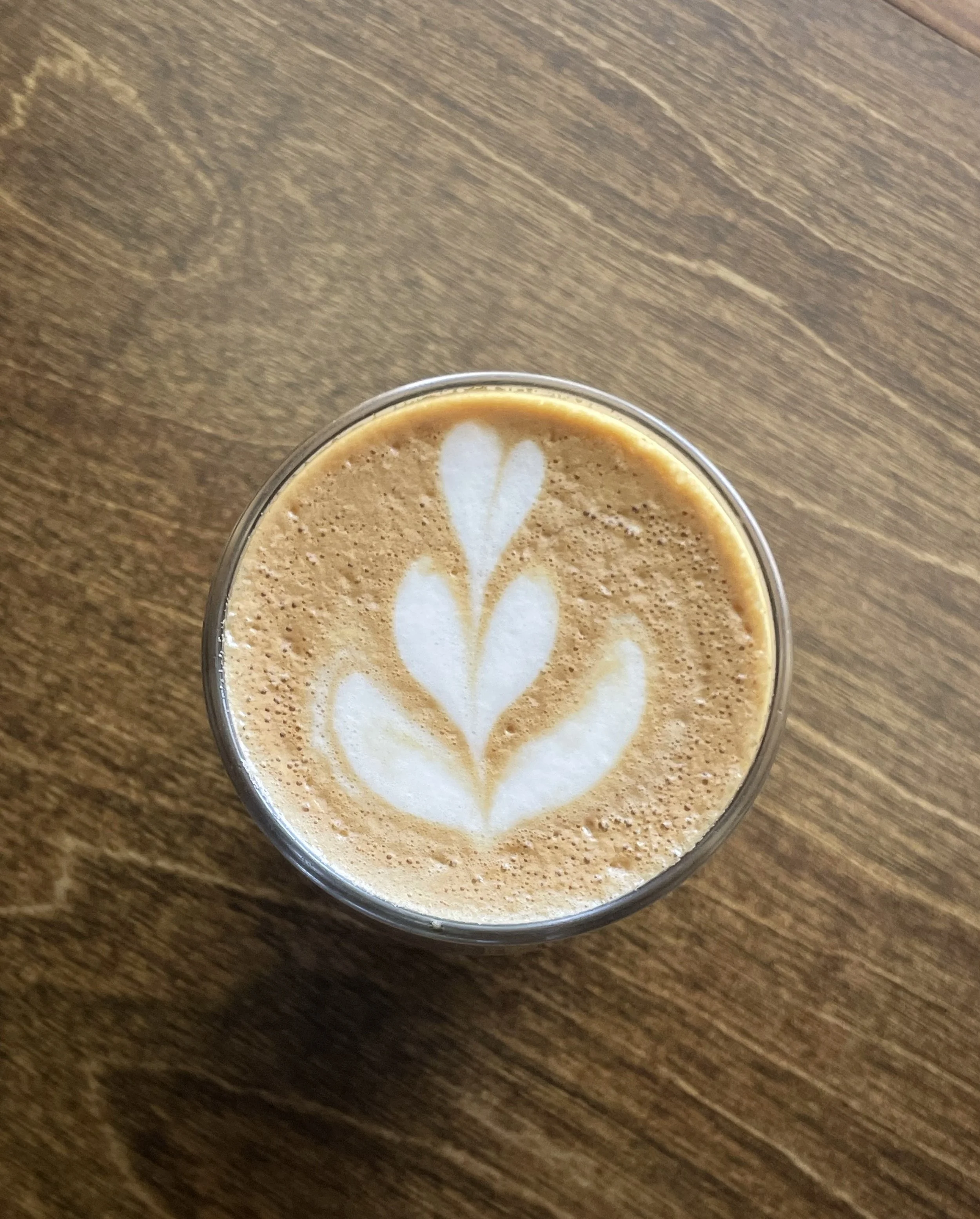 Top view of a glass of coffee with latte art in the shape of a tulip on a wooden table.
