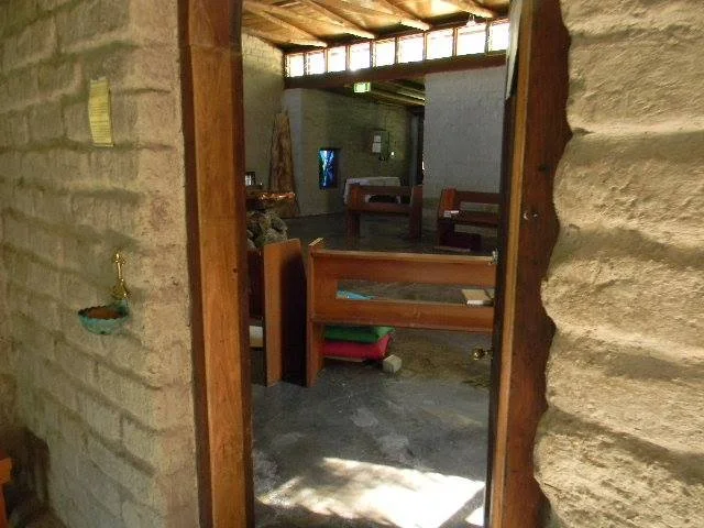 Interior of a small church or chapel with wooden pews, stone walls, and a window letting in natural light.