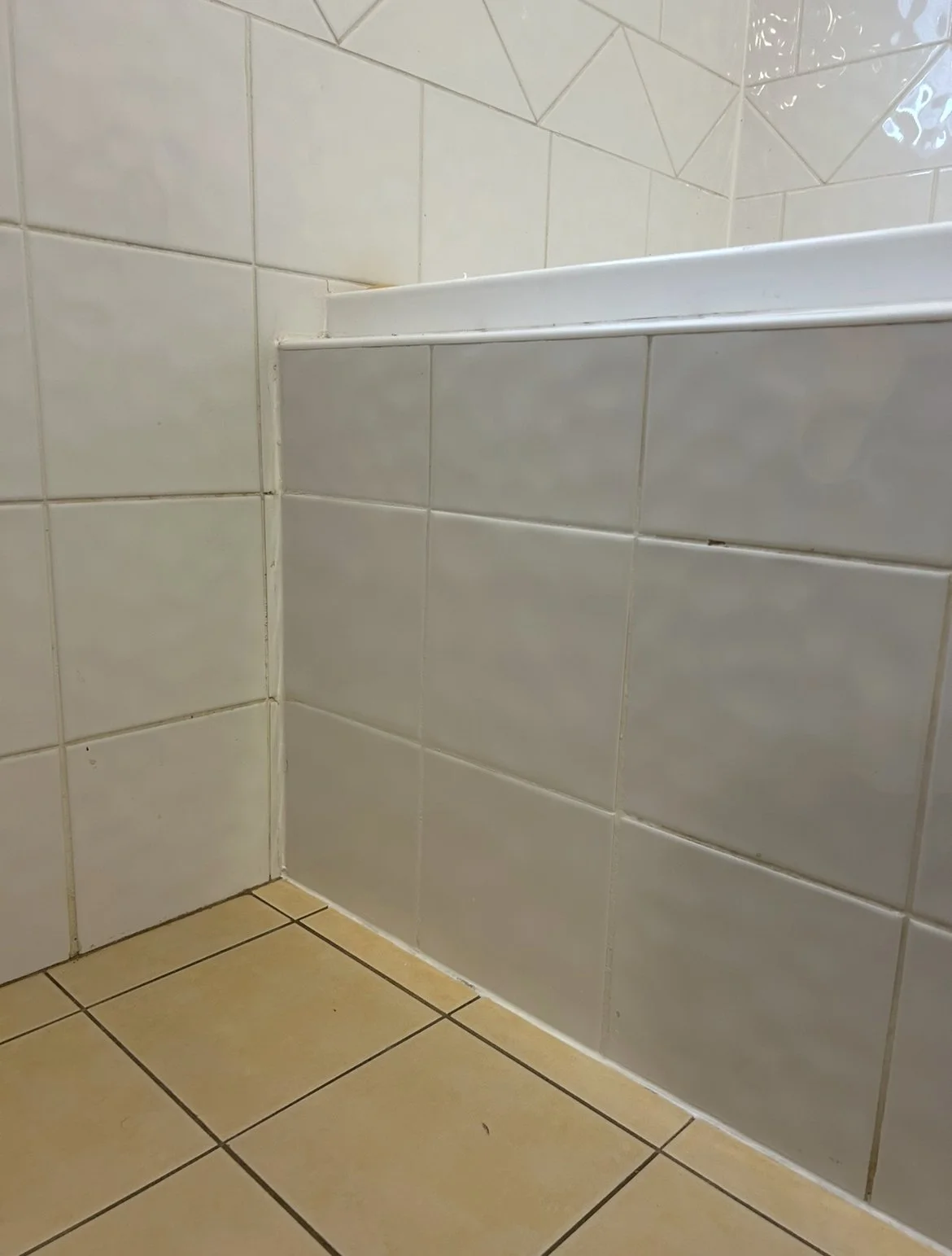 Close-up of a corner near a shower with white tiled walls and beige tiled floor.