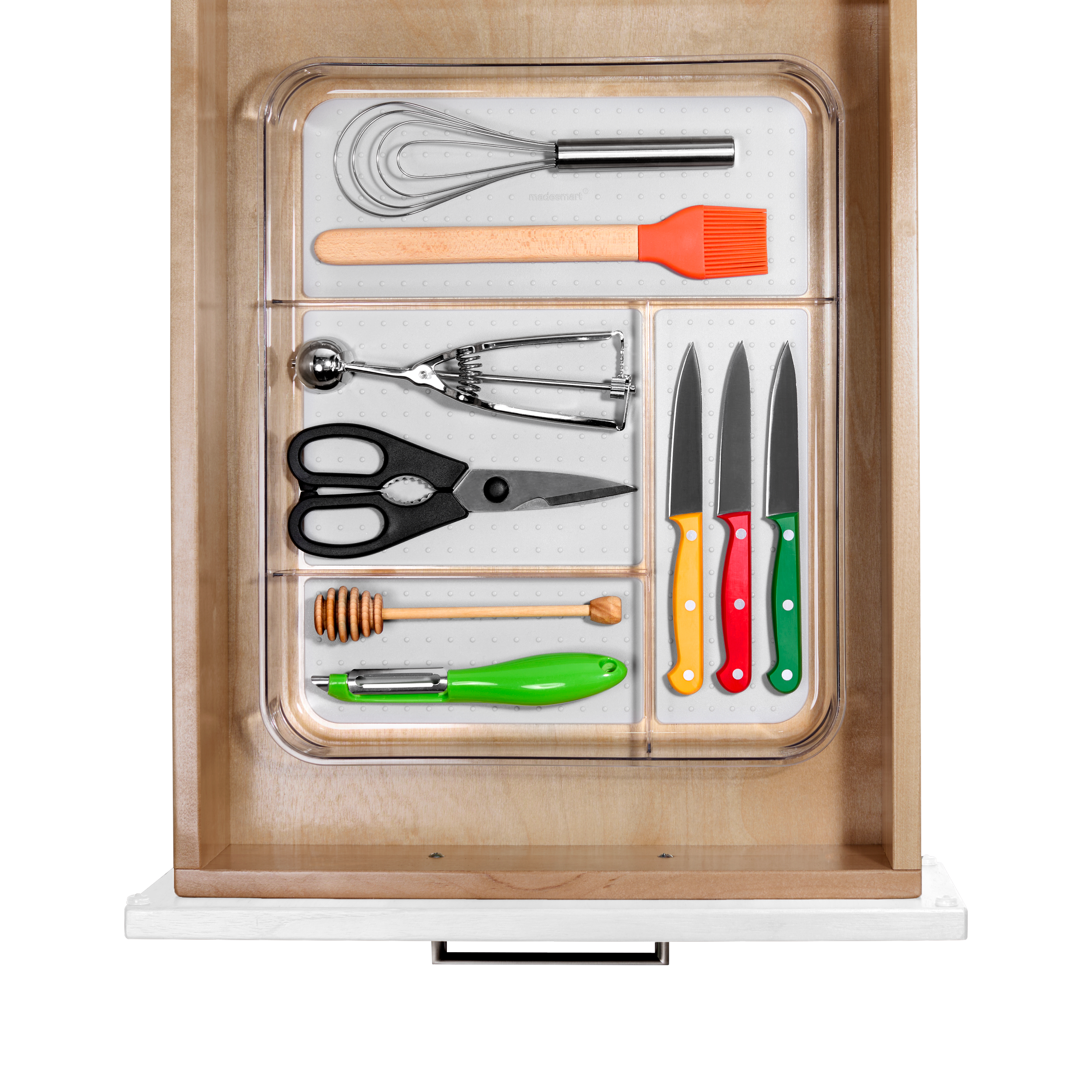 Drawer with kitchen utensils including whisks, spatula, scissors, knife set with yellow, red, and green handles, honey dipper, and vegetable peeler.