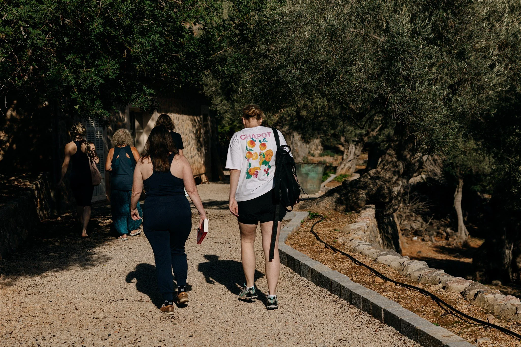Group of women walking on a dirt path surrounded by trees and stone walls.