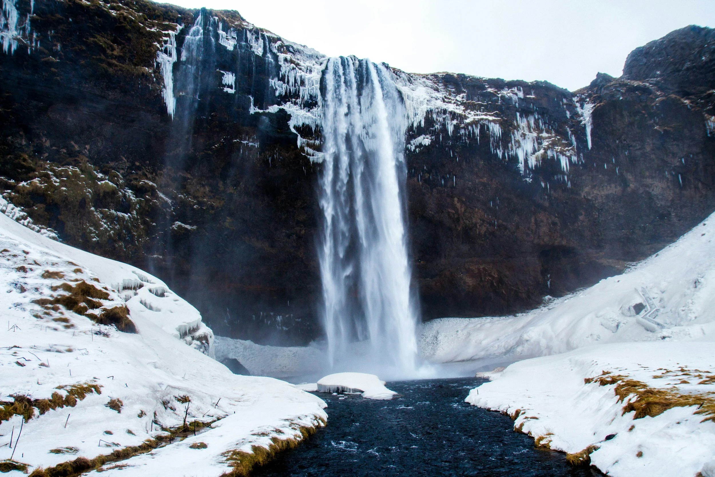 A waterfall cascading down a cliff into a river below, with snow and ice covering the surrounding landscape.