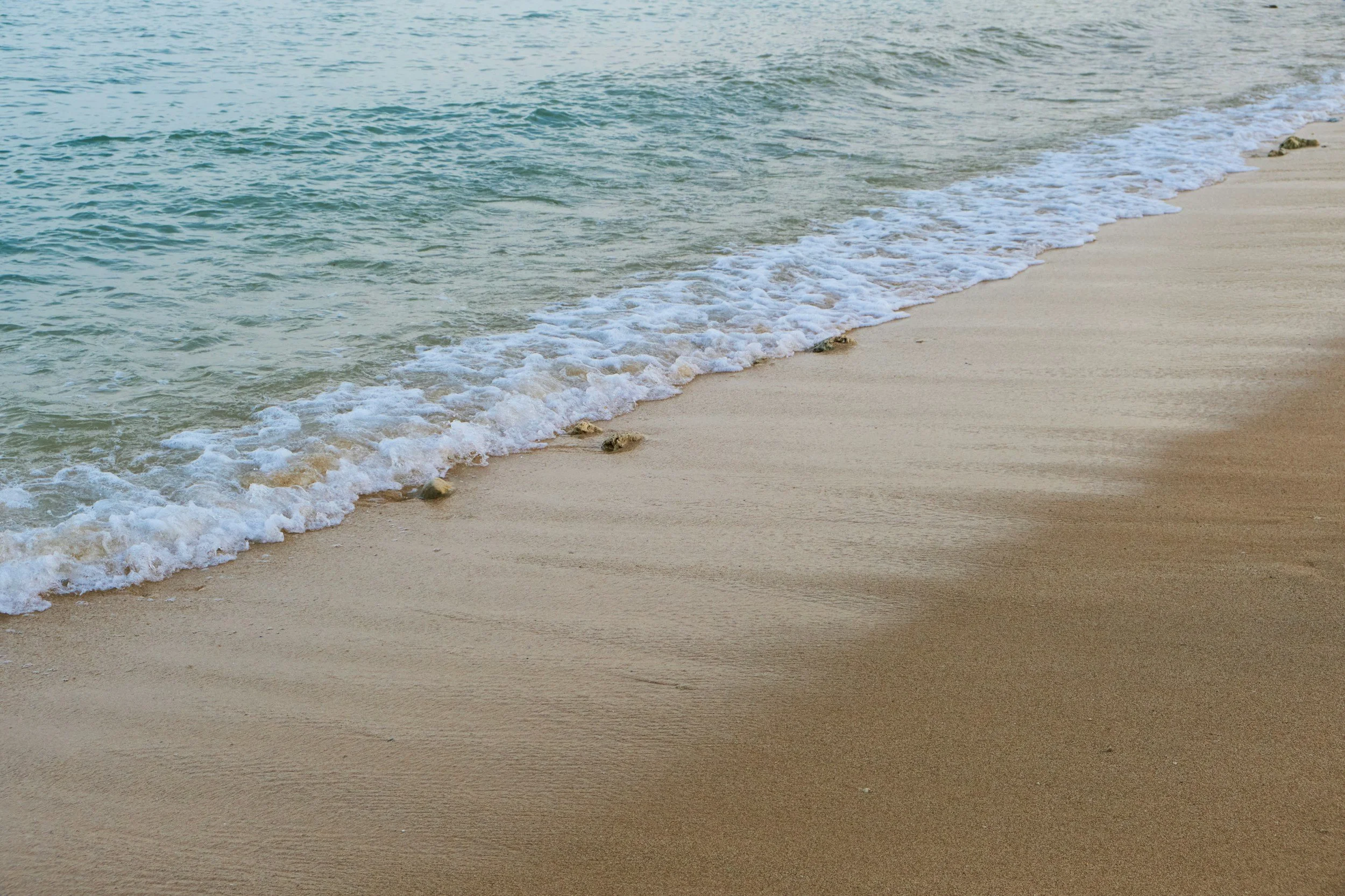Calm ocean waves lapping onto a sandy beach with ripples and small rocks.