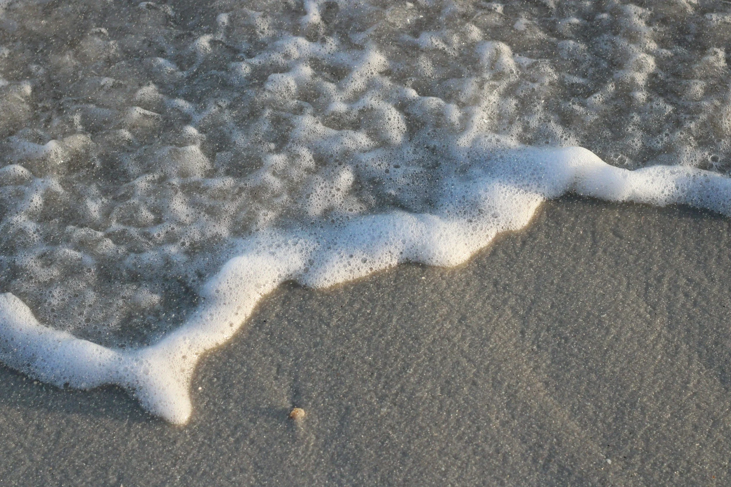 Close-up of ocean wave foam on sandy beach.