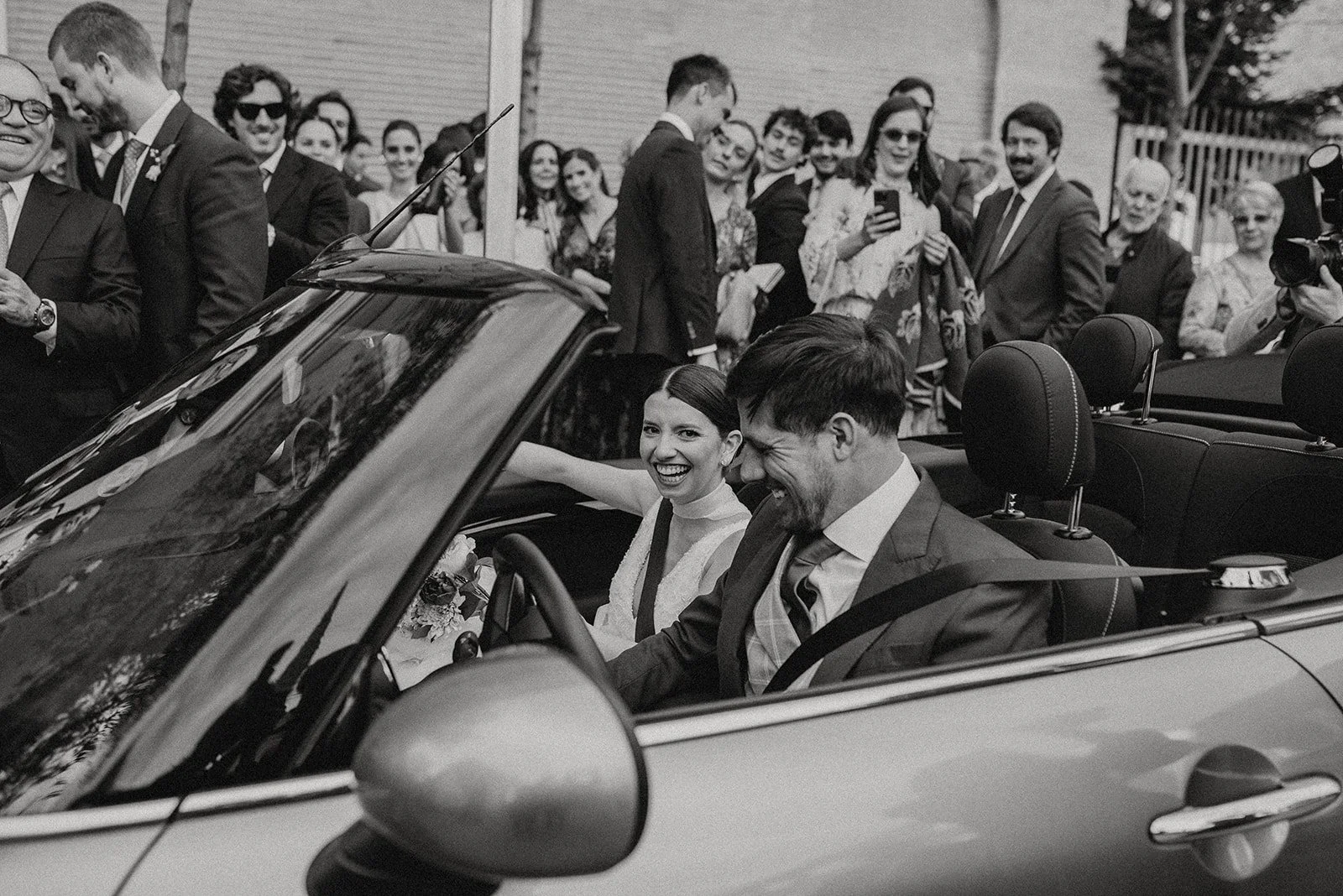 Pareja de recién casados en coche clásico rodeados de familia y amigos celebrando boda. Madrid. Elegancia