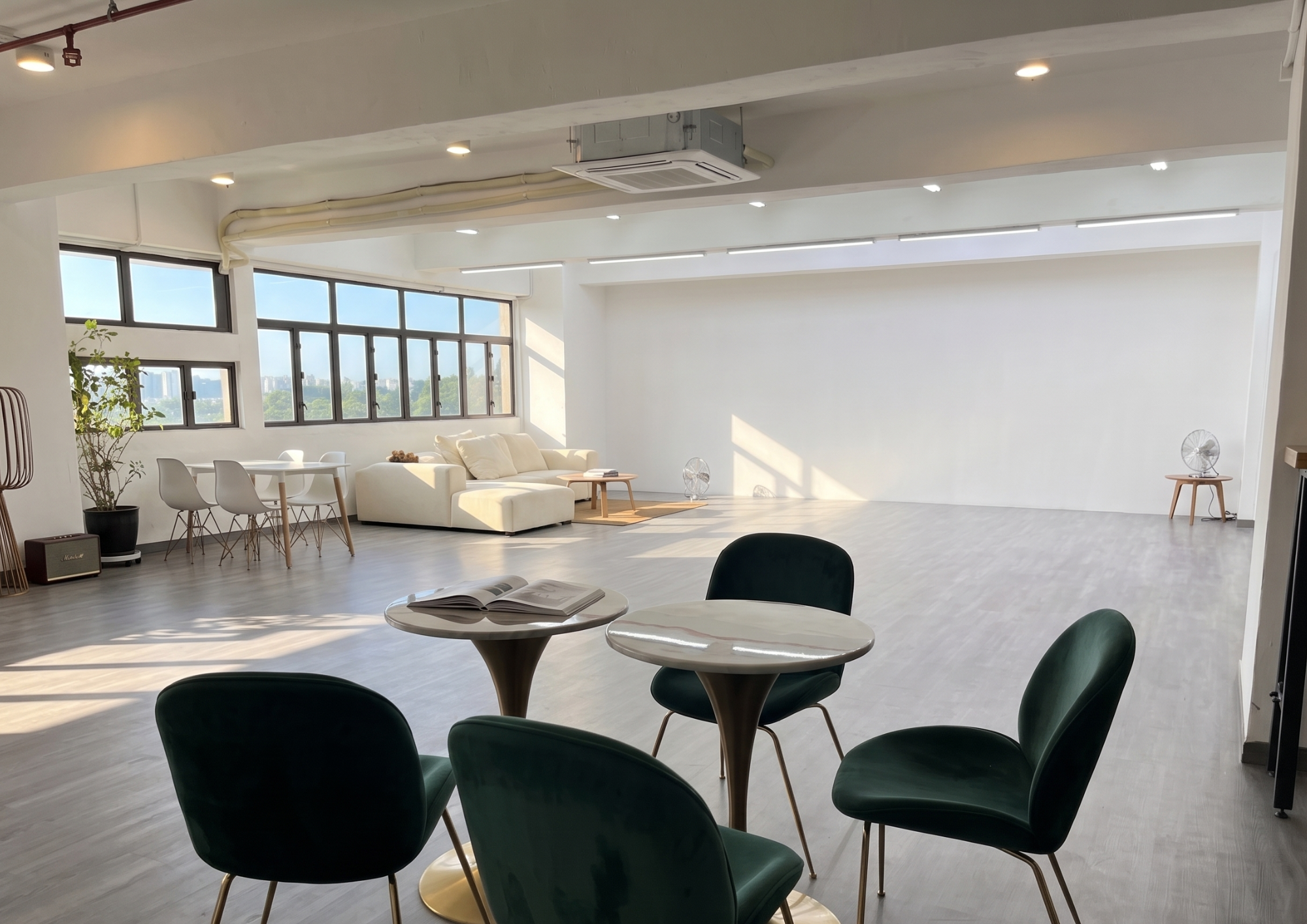 A bright lifestyle setup with lounge furniture, round catering tables, and black chairs illuminated by large windows.