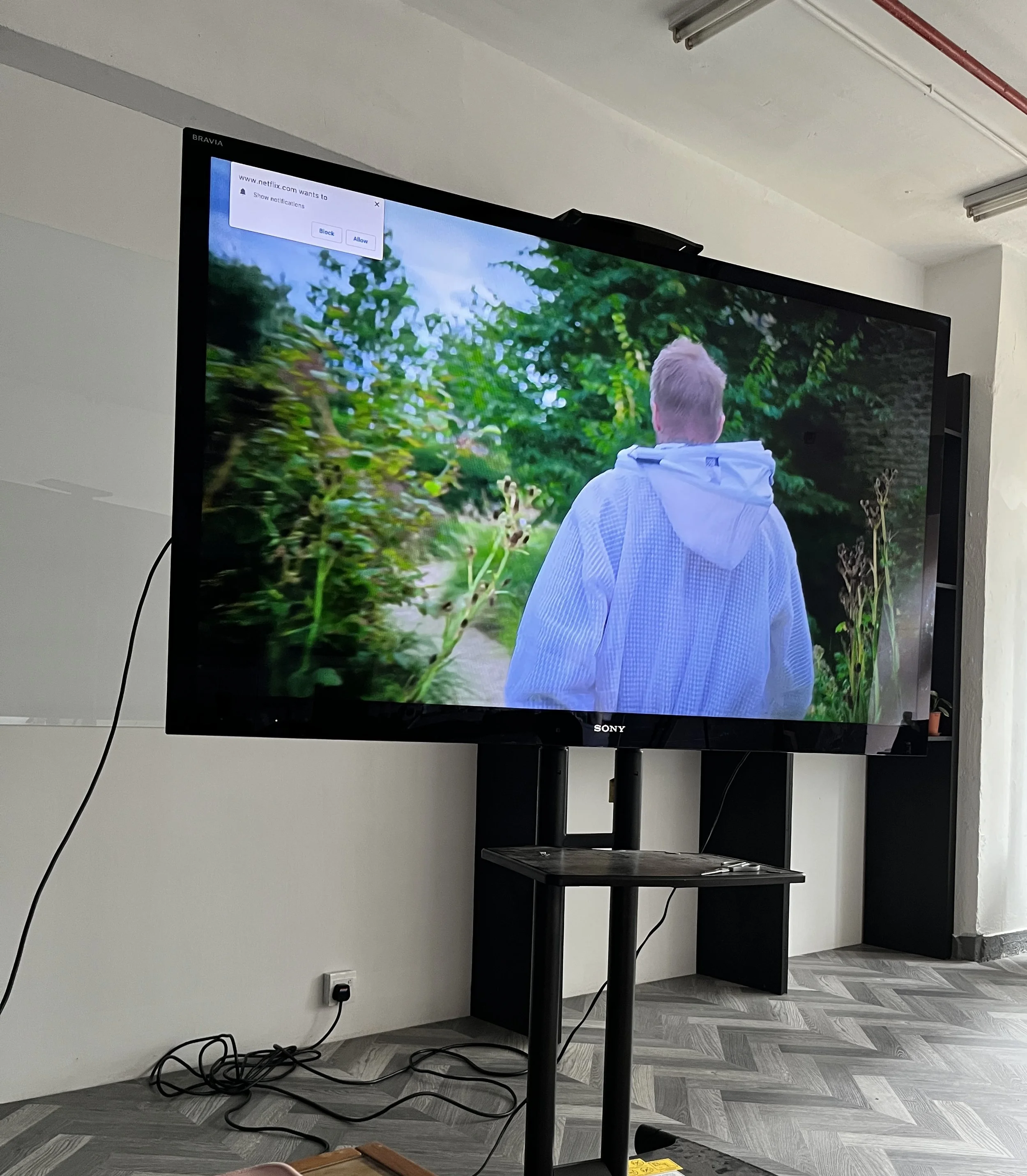 A large 60-inch mobile TV monitor display on a stand, part of the audio-visual equipment provided for corporate presentations and meetings at The Hang.