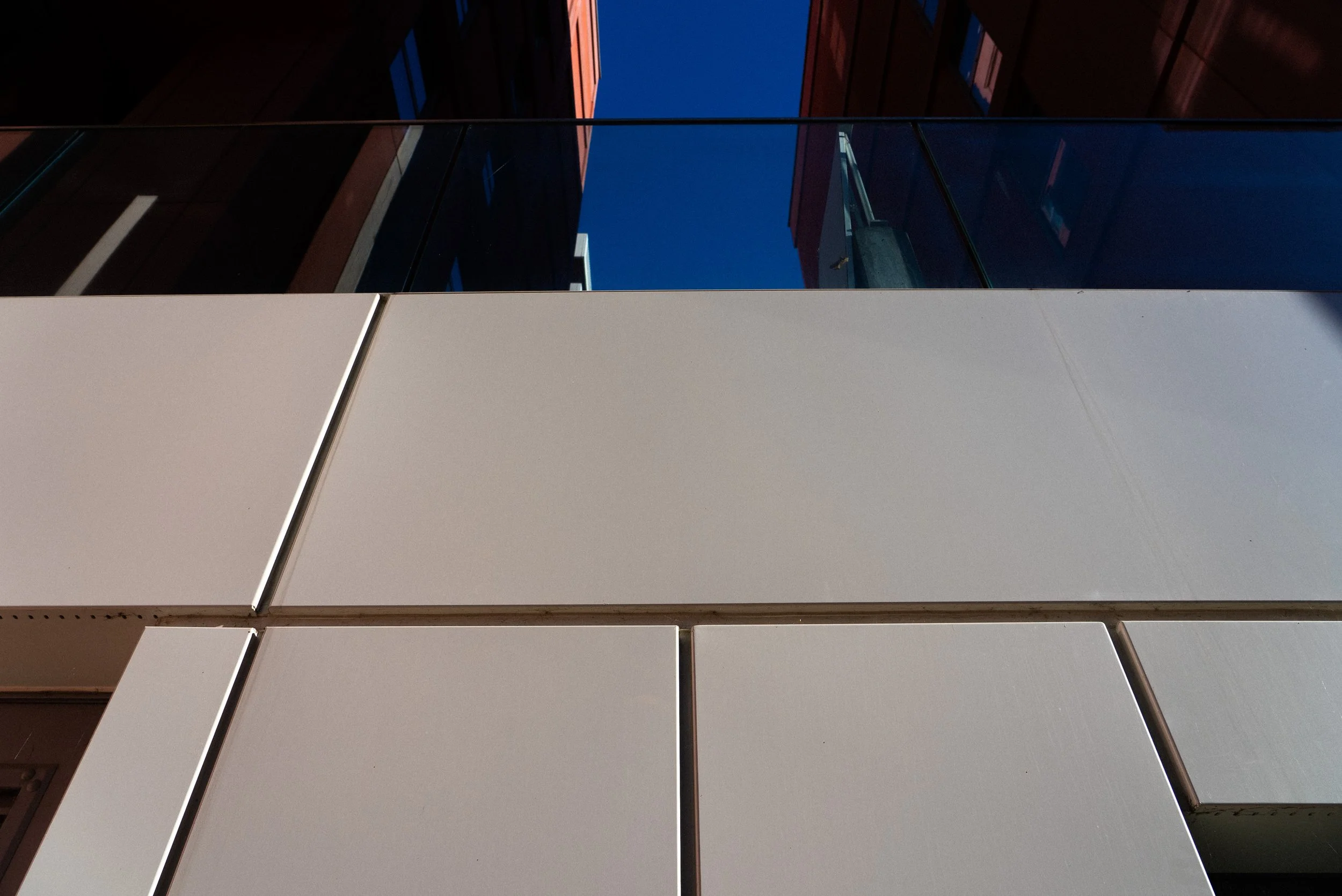 Close-up shot of building modern white facade with glass windows reflecting a clear blue sky.