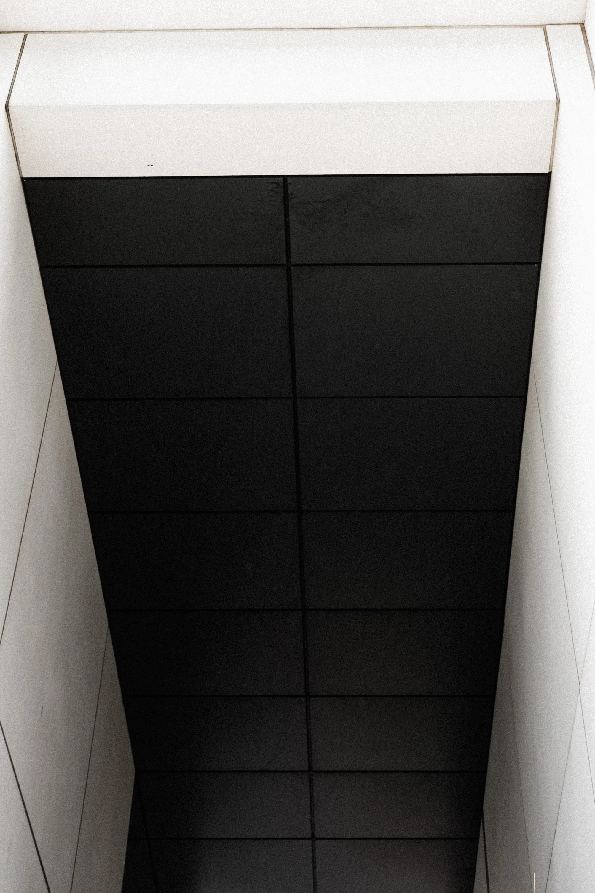 Ceiling with black square tiles and white side walls in a modern architectural space.