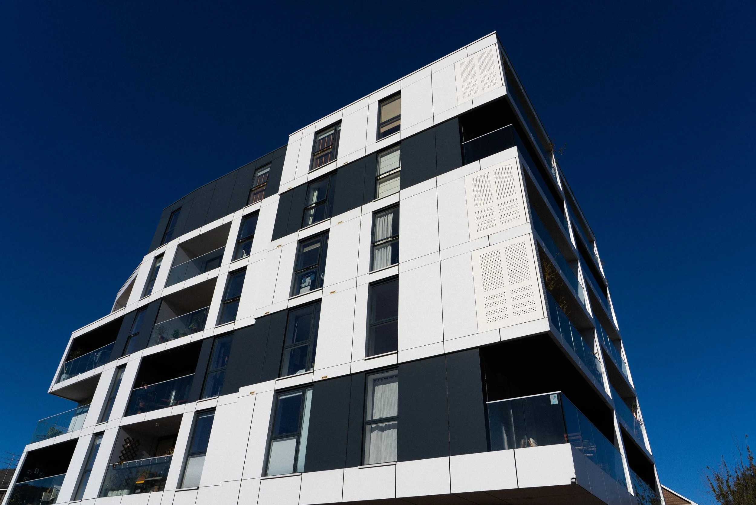 Modern multi-story apartment building with white and dark panels under a clear blue sky.