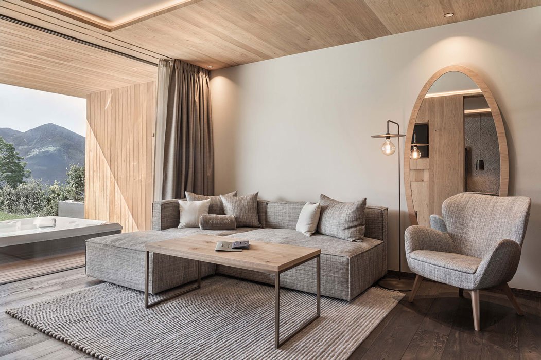 Modernes Wohnzimmer mit grauem Sofa, Sesseln und Holzmöbeln, Blick auf die Berge, offene Balkontür.