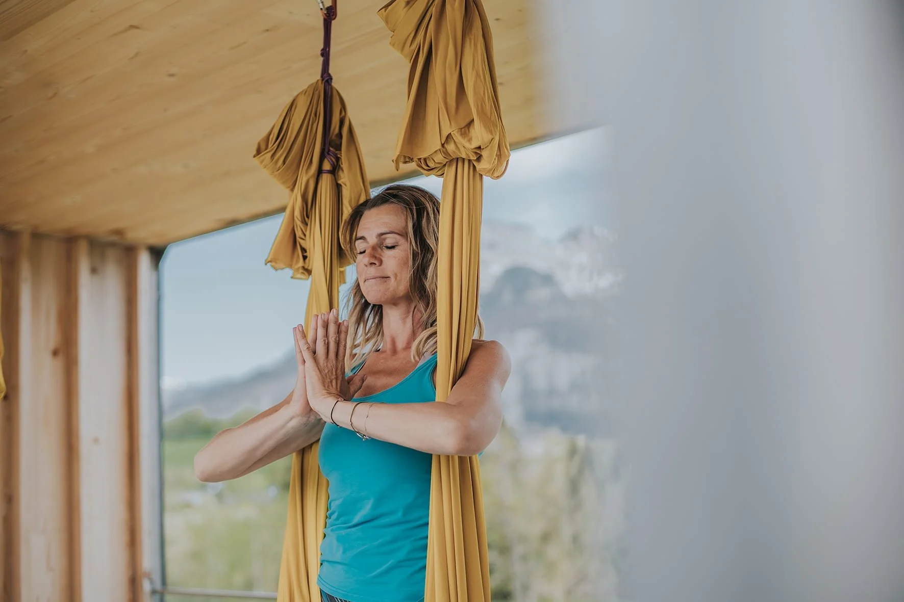 Frau macht eine Yogaübung an einem Aerial Yoga Tuch, mit Blick auf Berge und Himmel im Hintergrund.