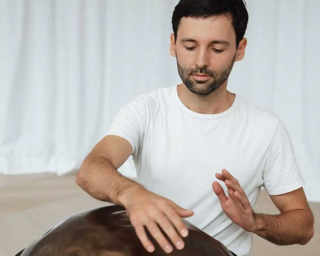 Ein Mann spielt mit einer Handpan, sieht entspannt aus.