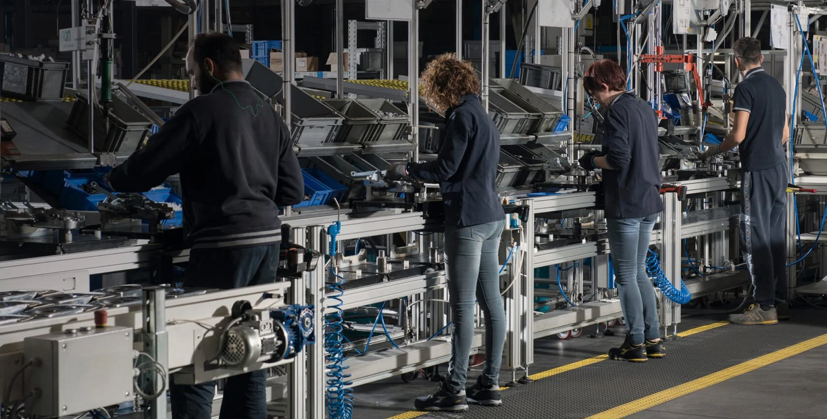 Fyras personer arbetar på en automatiserad produktionslina i ett industrilabb, alla är fokuserade på sina uppgifter.