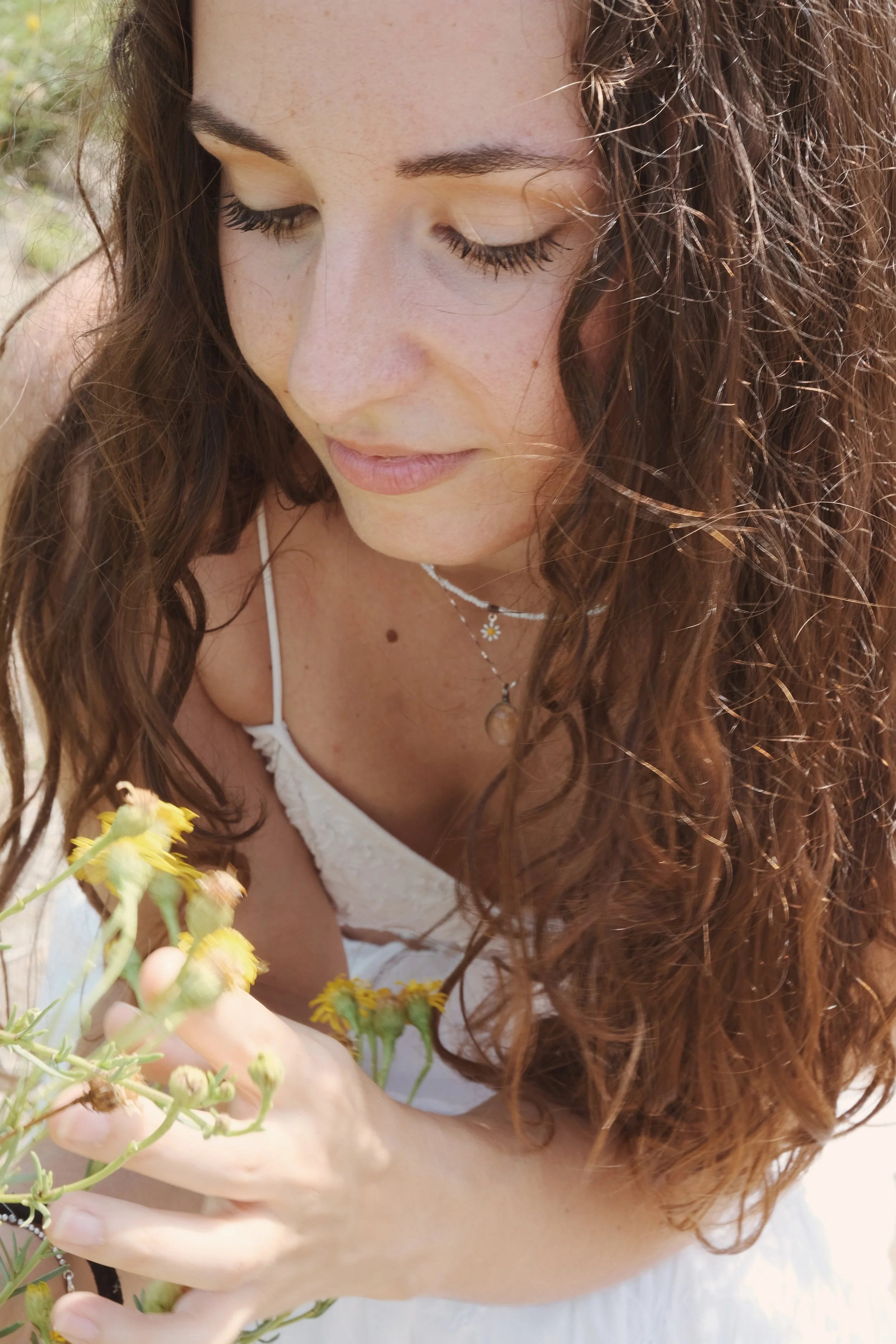Una donna con capelli ricci marroni chiari che raccoglie fiori gialli.