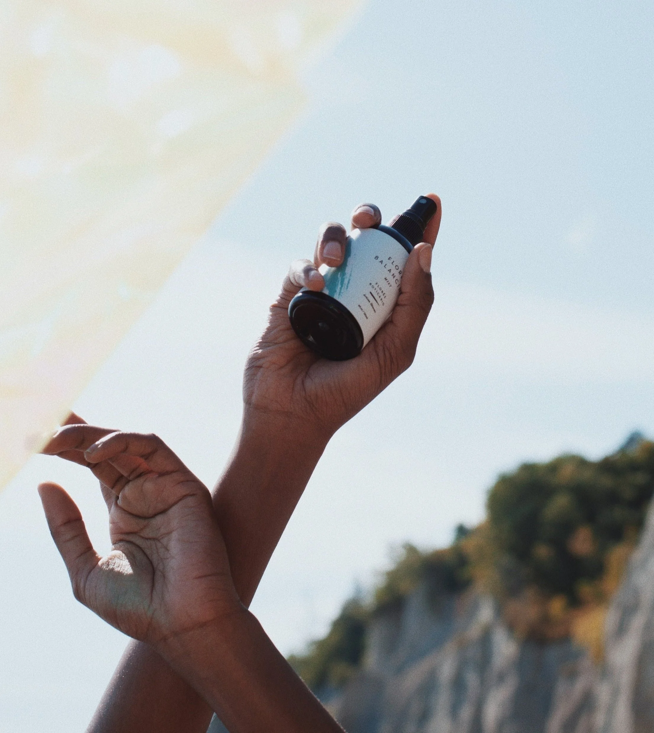 Person holding spray bottle against sky and cliff backdrop