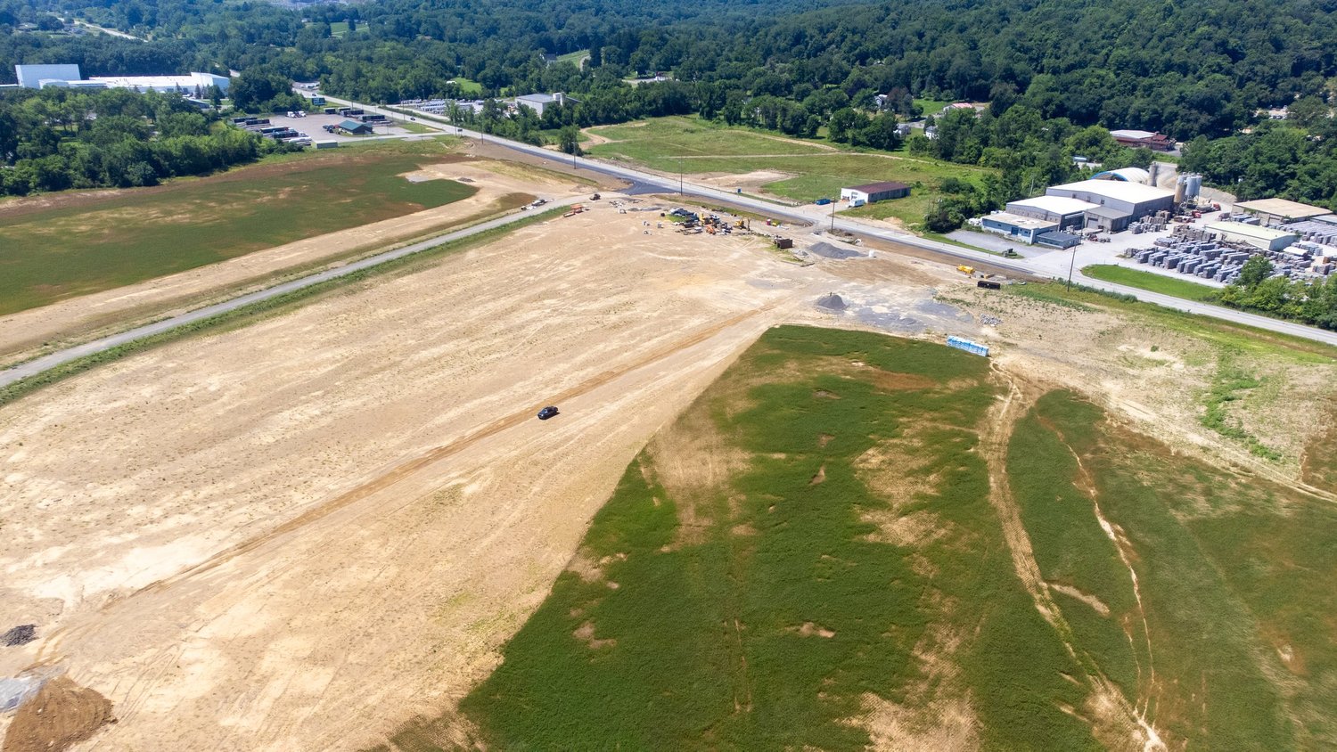 Aerial view of a construction site with cleared land, some grass patches, and construction equipment.