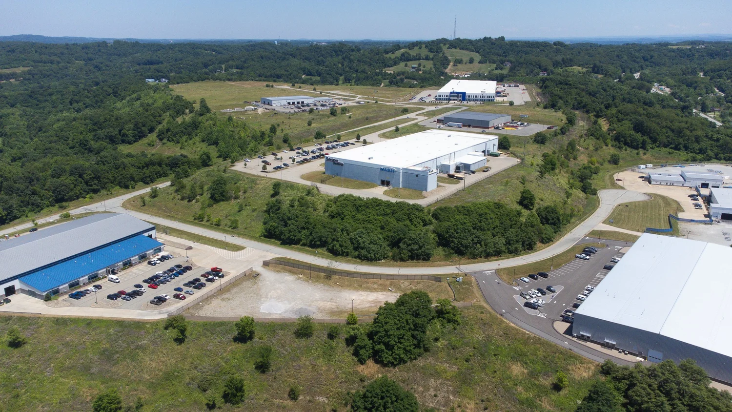 An aerial view of an industrial complex with multiple large warehouse buildings, parking lots full of cars.