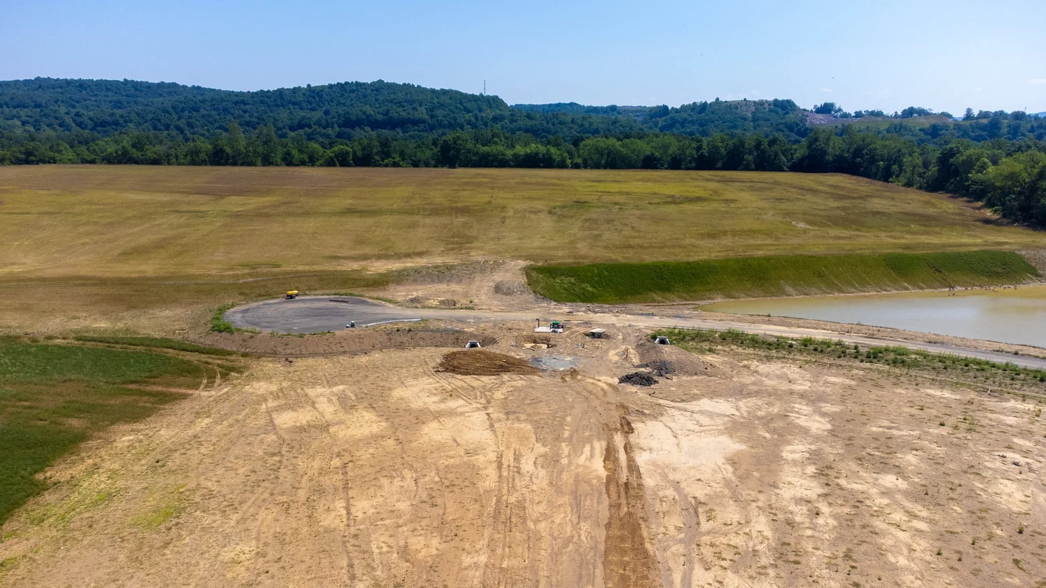 Construction site in a rural area with cleared land, construction equipment, a pond.