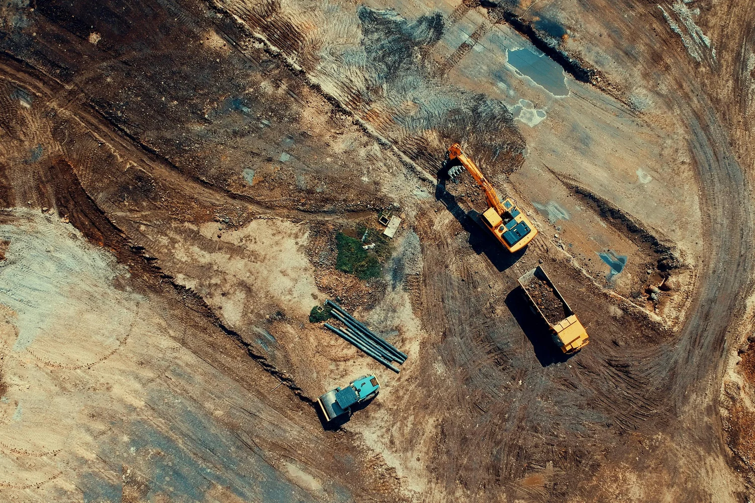 Aerial view of an active construction site with yellow excavators and trucks on bare earth.