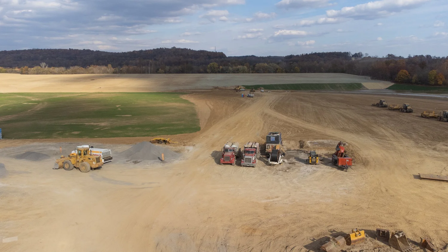 Construction site with several bulldozers and trucks working on earth excavation.