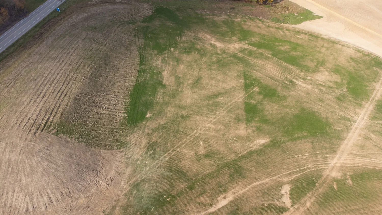Aerial view of an open field with patches of green grass and areas of bare soil.
