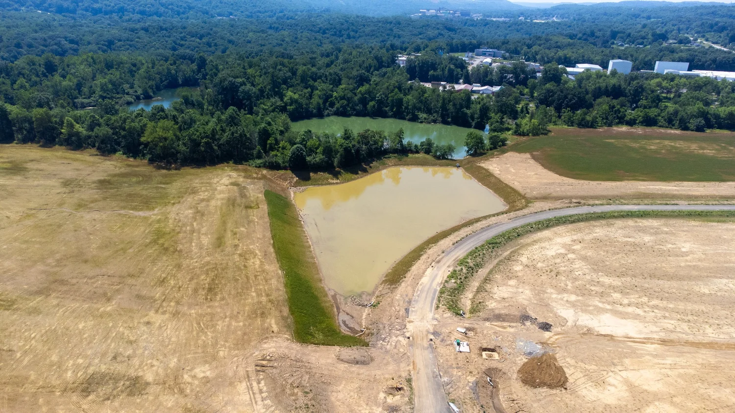 Aerial view of a construction site with cleared earth and a small pond.