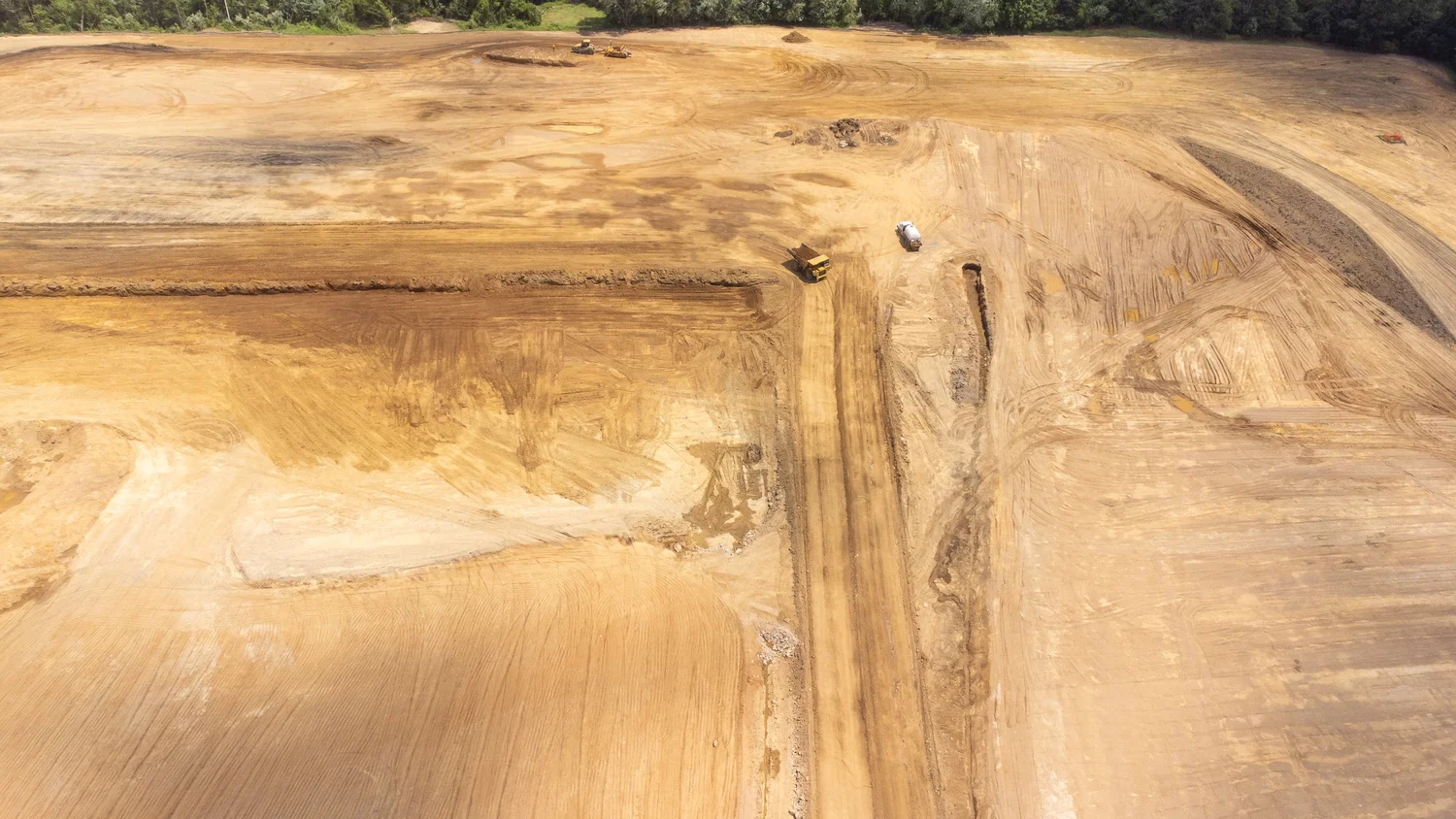 Aerial view of a construction site with dirt roads, machinery, and cleared land surrounded by trees.