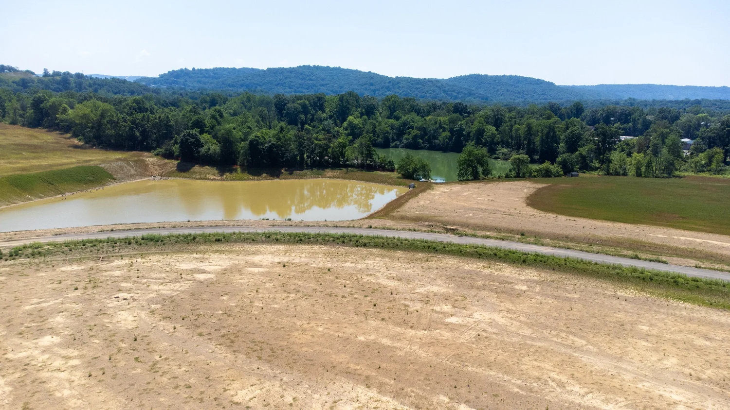 Scenic landscape with hills, trees, a small pond, and dry grass areas, under a clear blue sky.