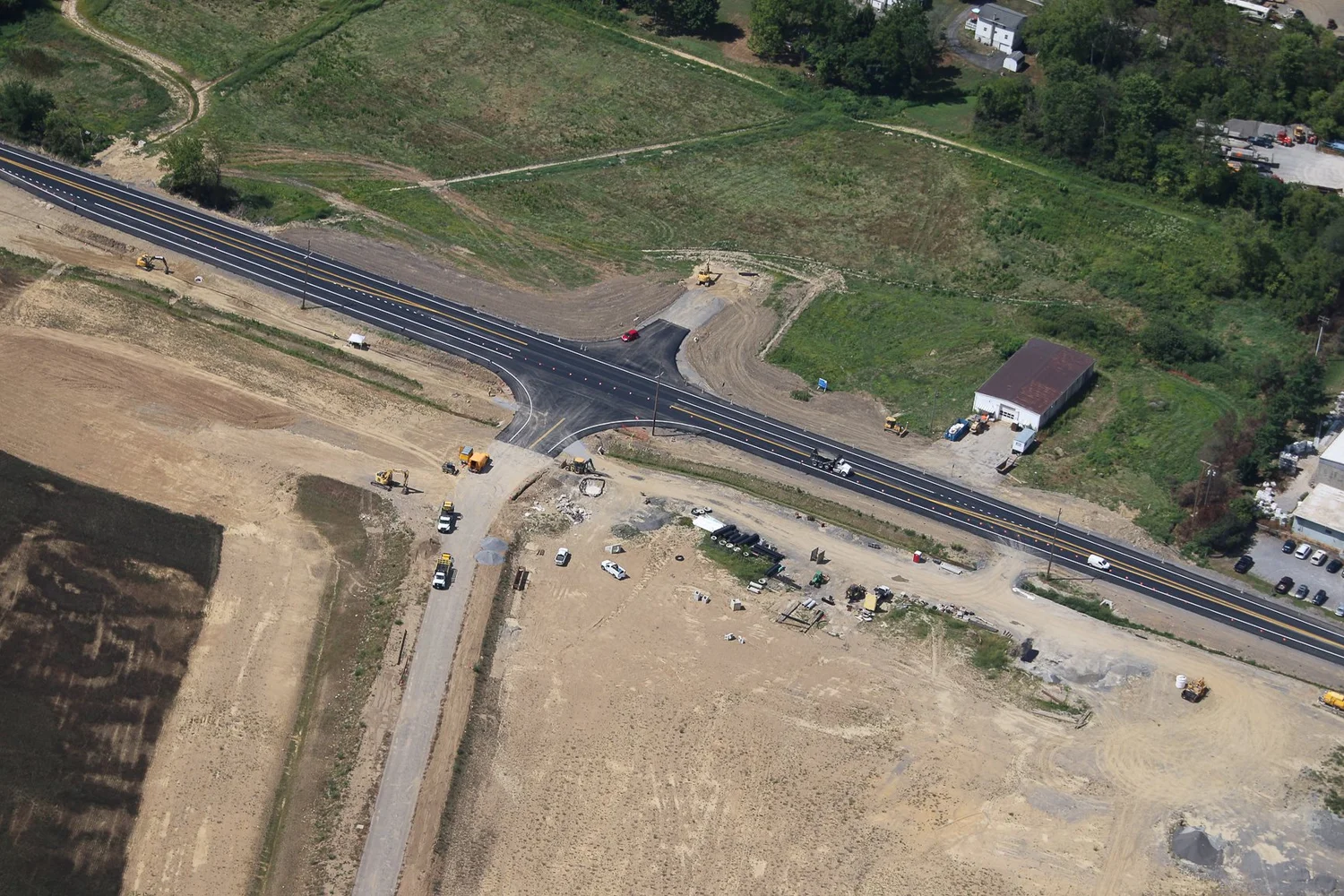 Construction site on a road with several construction vehicles, equipment, and a newly paved section of highway.