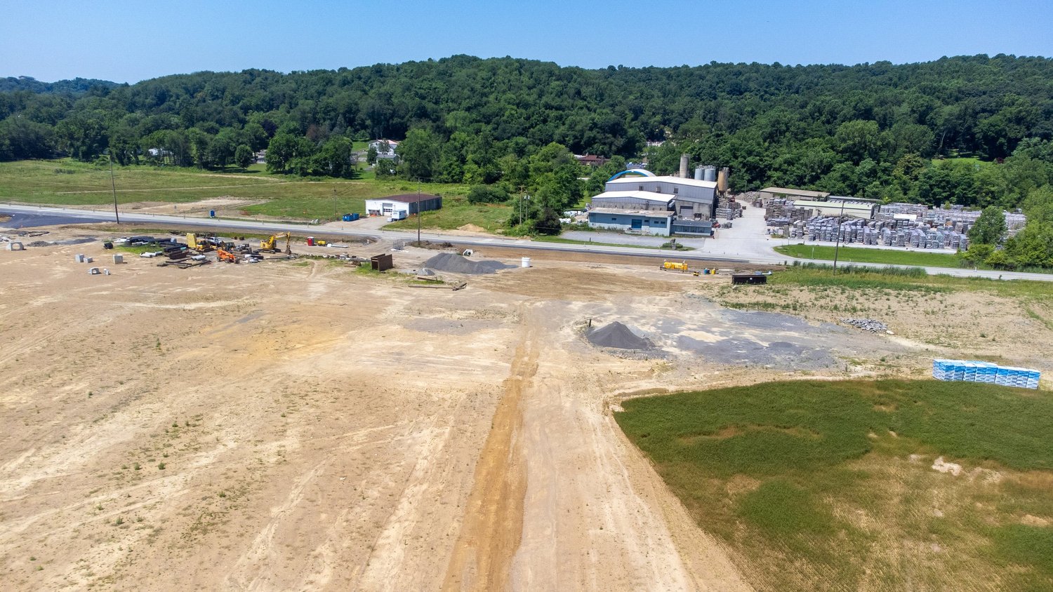 Construction site with machinery, dirt paths, and piles of materials, with a building and storage area in the background.