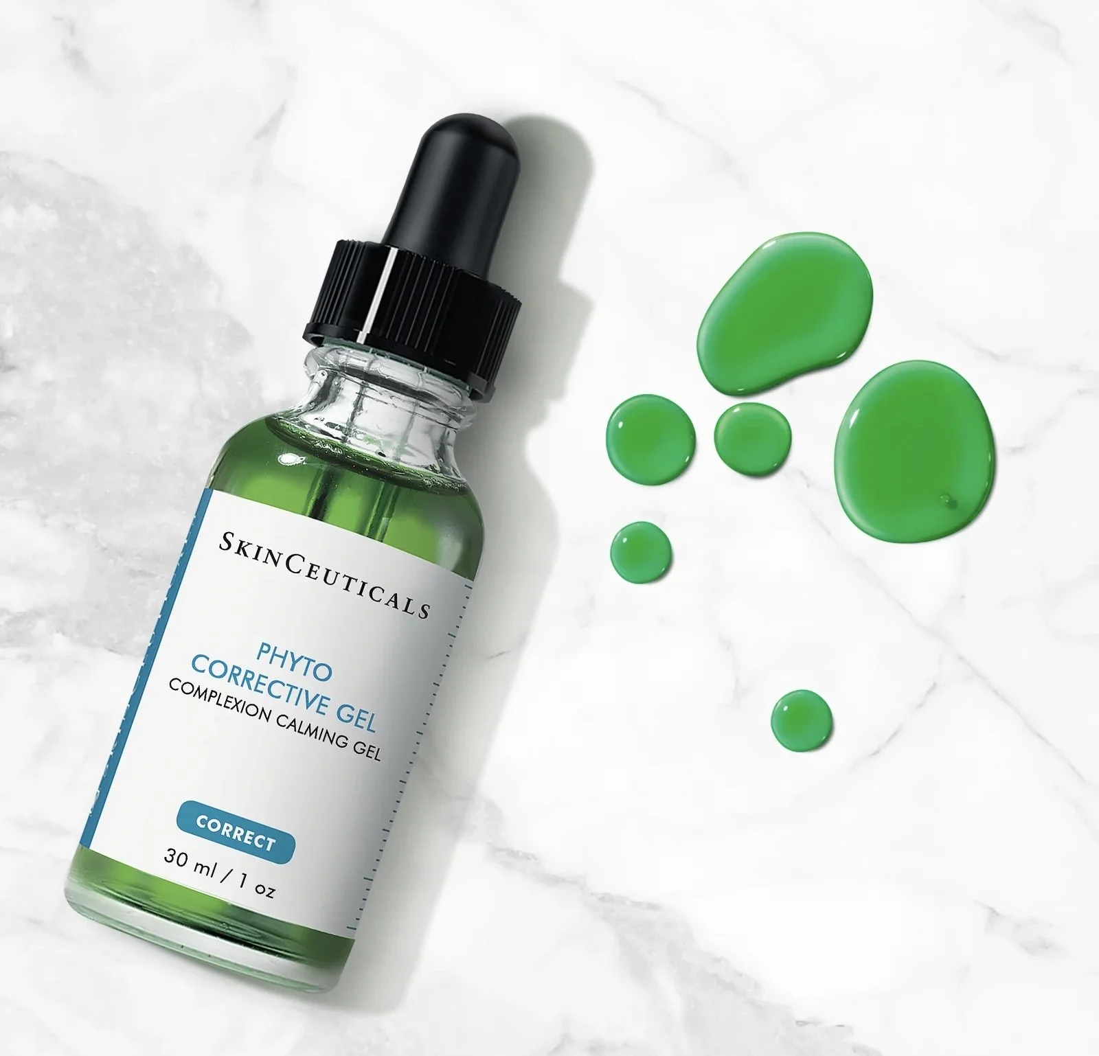A bottle of skin care product labeled Skinceuticals Phyto Corrective Gel with green gel drops on a white marble surface.