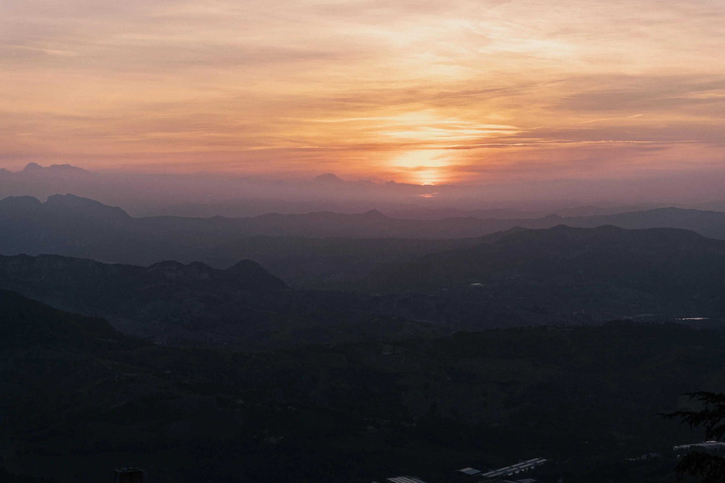 Berglandschaft bei Sonnenuntergang mit mehrschichtigen Bergen und einem farbigen Himmel.