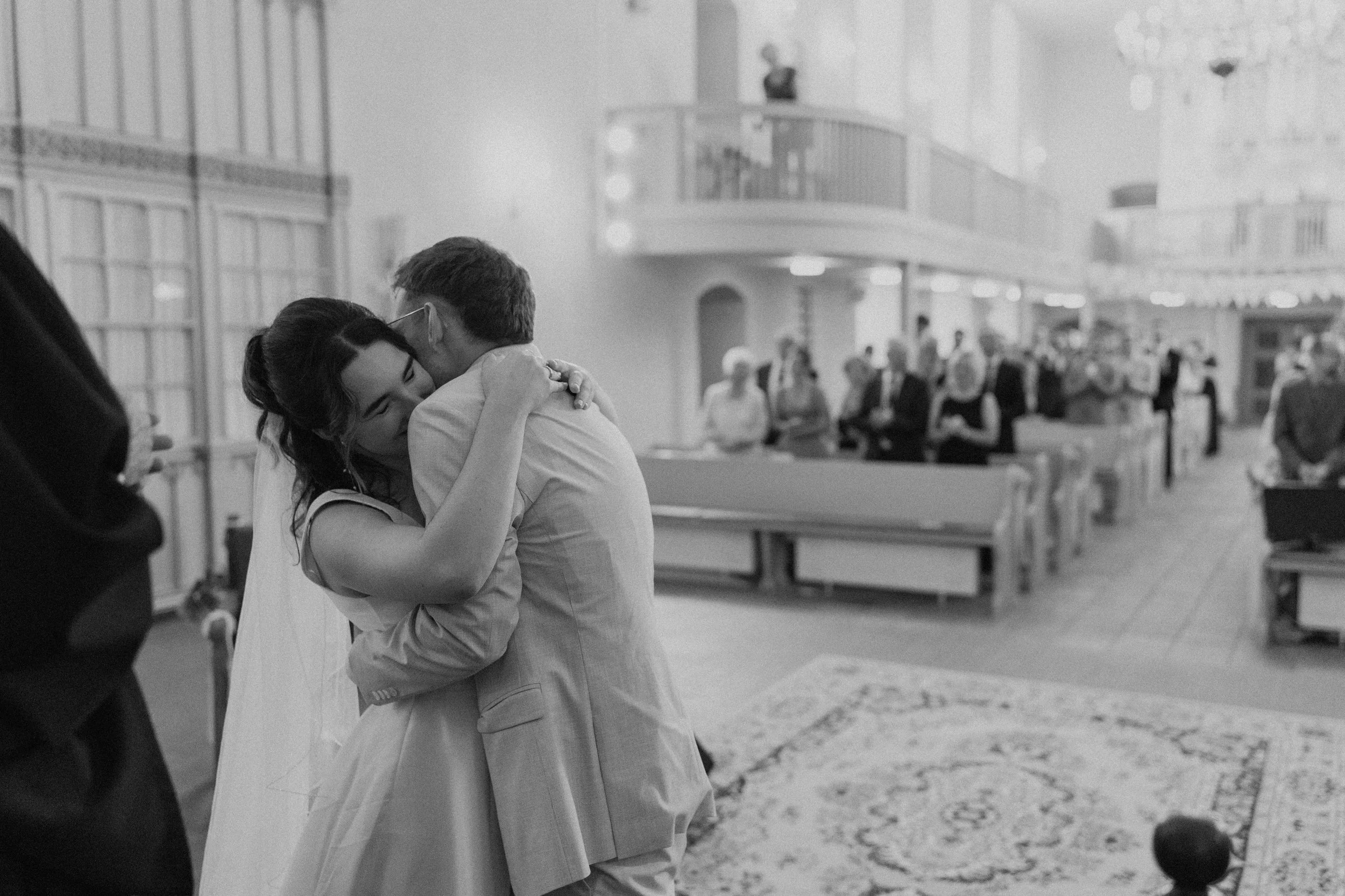 Ein Brautpaar umarmt sich in einer Kirche während einer Hochzeitszeremonie, umgeben von Gästen.