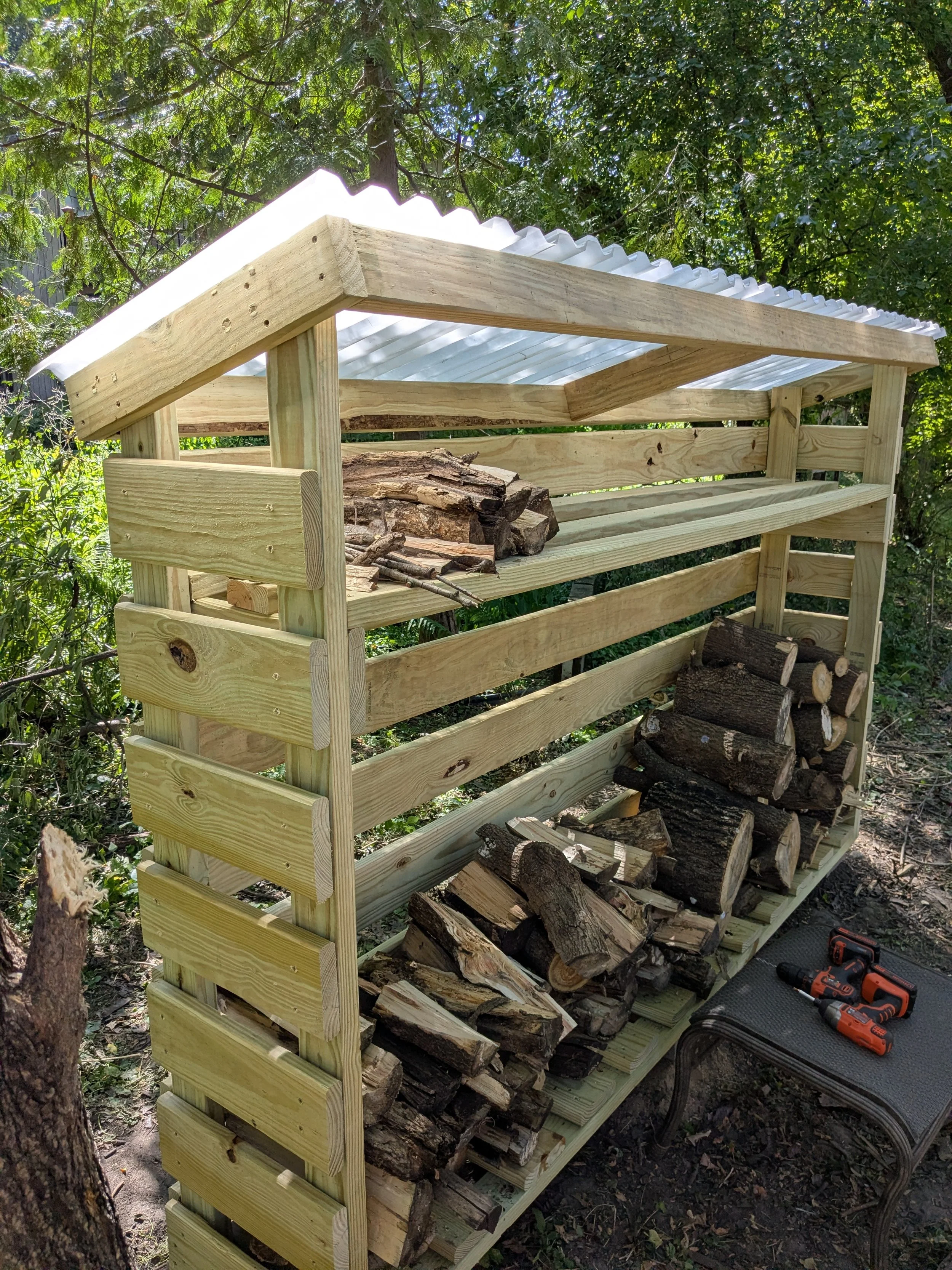 Finished DIY firewood shed loaded with split hardwood, slat sides and translucent corrugated roof