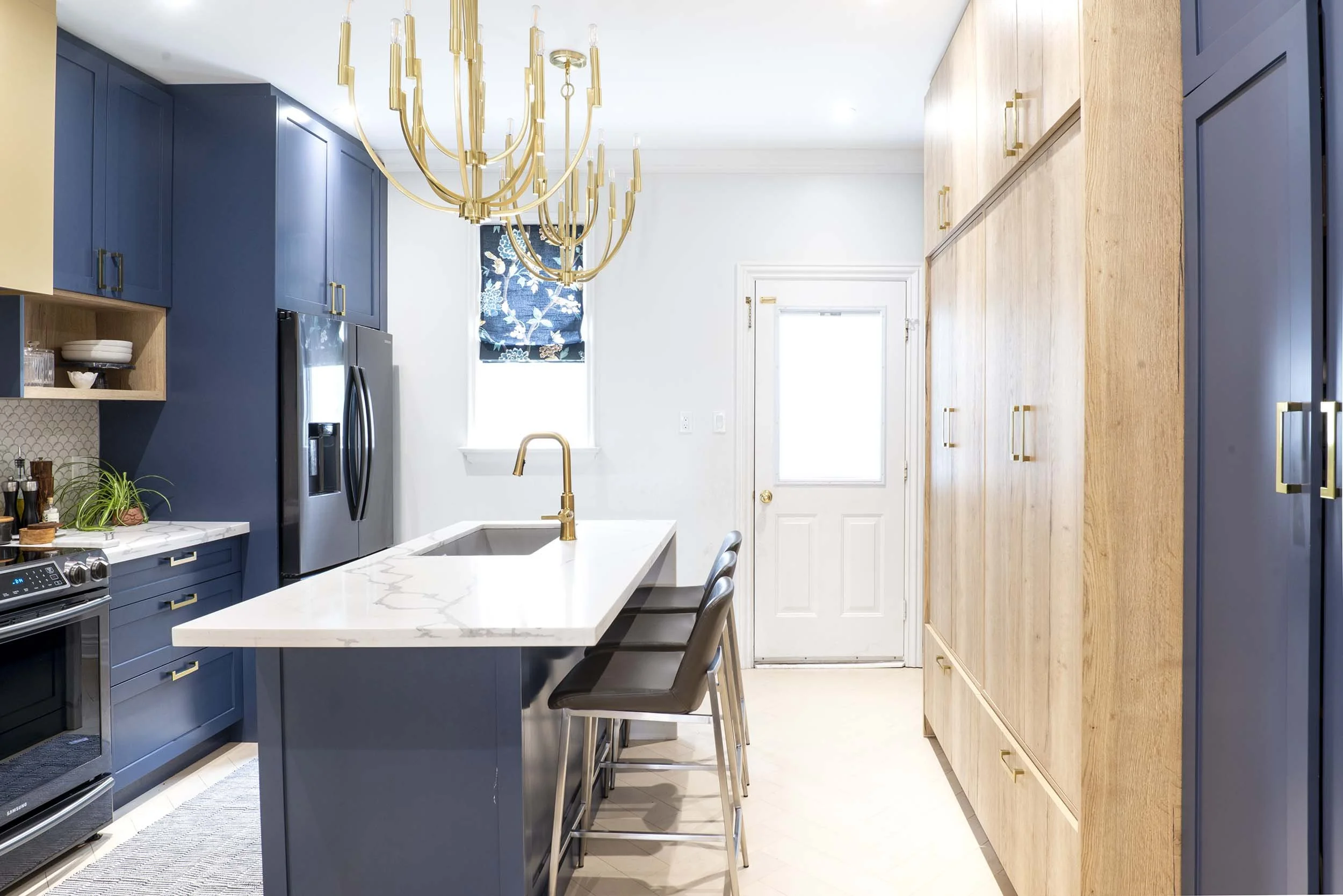 Navy blue cabinetry with white marble countertops. Custom wood pantry spanning the full side of kitchen.