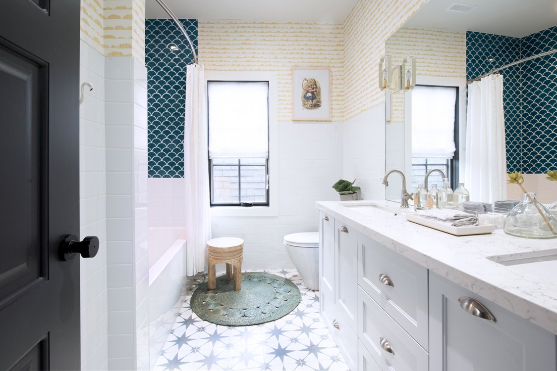 Modern bathroom with white cabinetry, marble countertop, blue scallop tile wall, patterned floor, and a round stool by the bathtub.