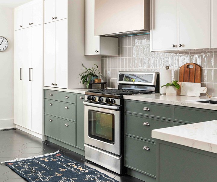 Modern kitchen with green cabinets, stainless steel stove, white countertops, and a patterned area rug.