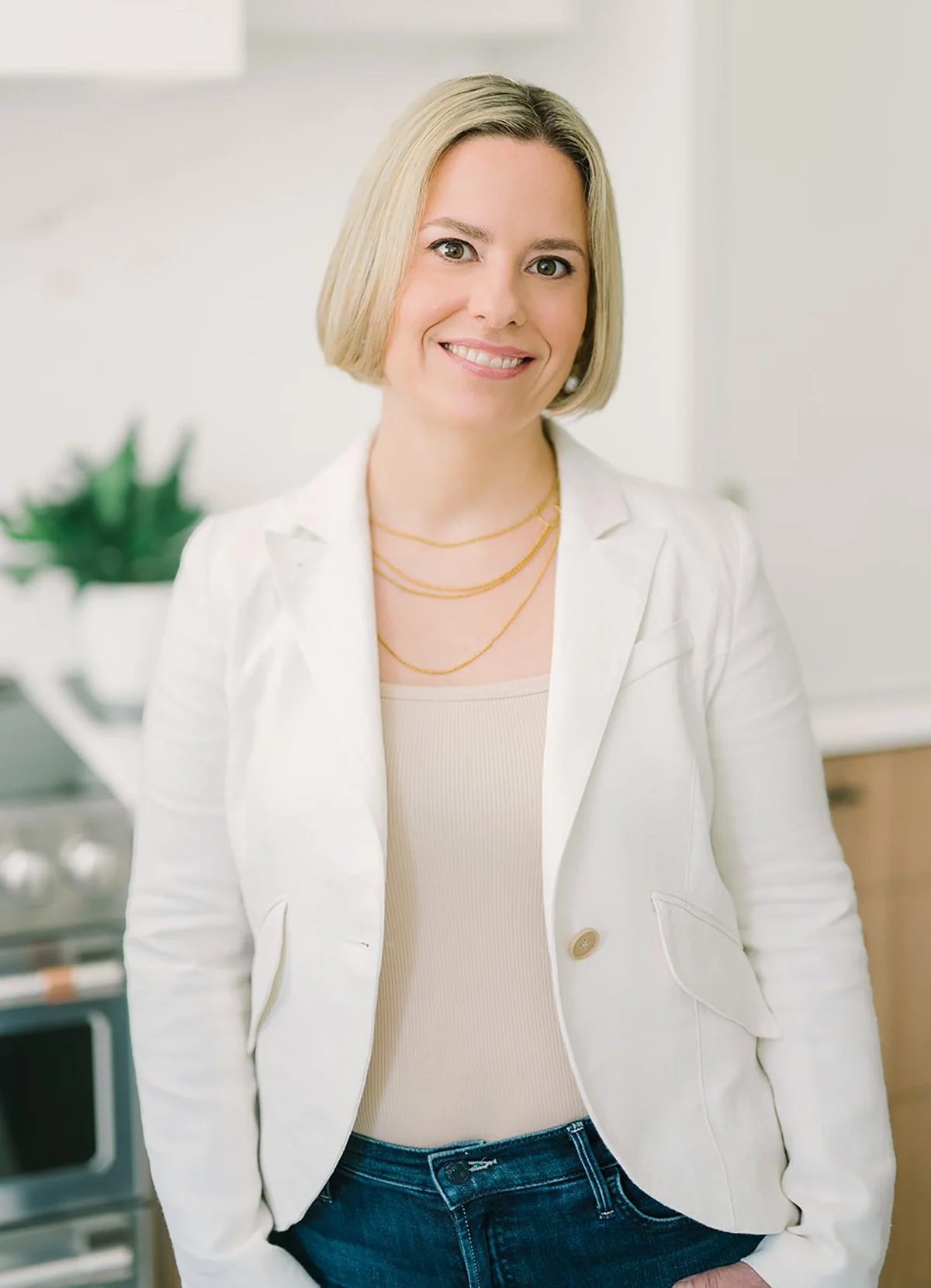 Confident woman in white blazer smiling in a kitchen setting.