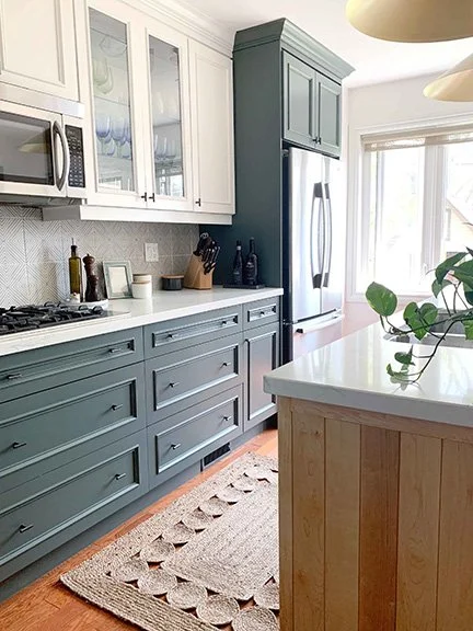 Kitchen with blue and white cabinetry, stainless steel refrigerator, microwave, and a white countertop with a plant on it.