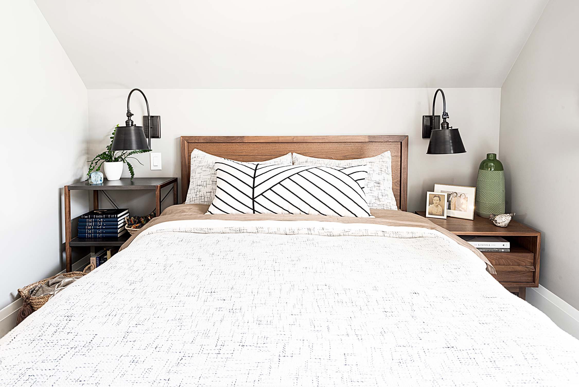 Bedroom with wooden bed frame, white and black striped pillows, and neutral bedding. Nightstands with decorative items, wall-mounted lamps, and framed photos.