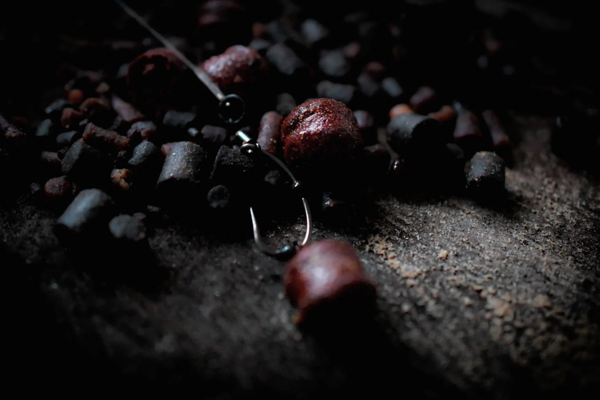 Close-up of scattered dark coffee coffee beans with a few red berries, with a pair of silver earrings with dark beads lying among them on a textured dark surface.