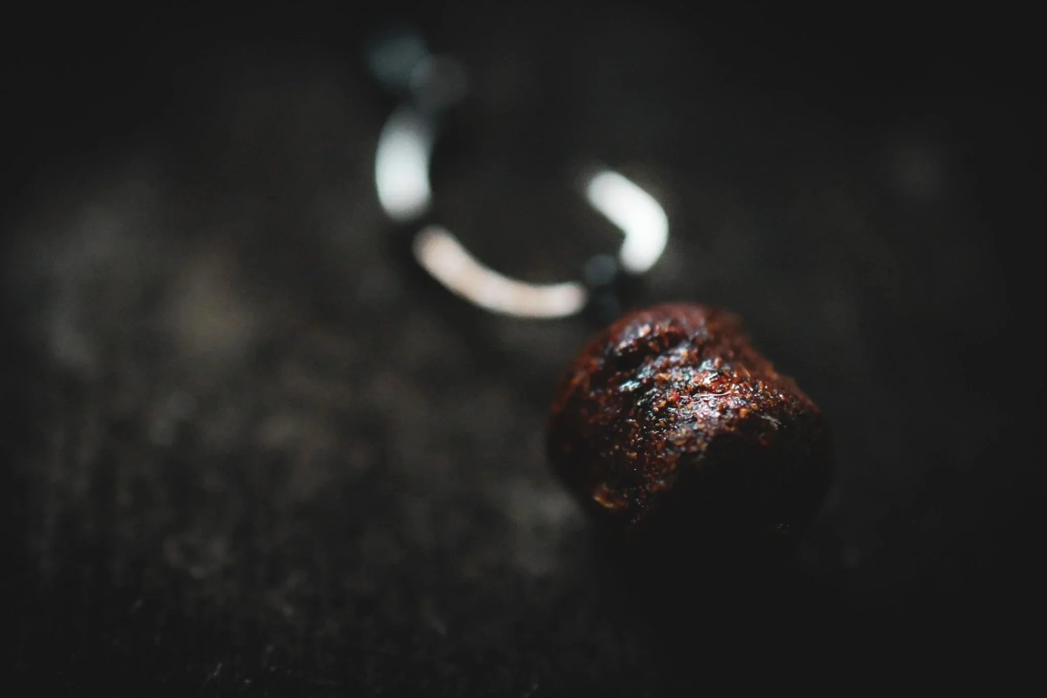 A dark background with a metallic ring and a polished, reddish-brown teardrop-shaped stone or mineral in the foreground.