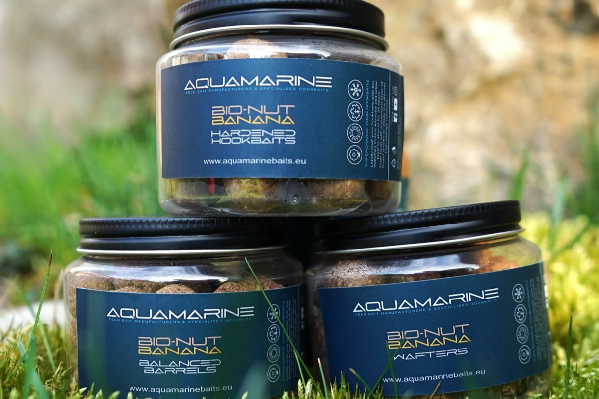 Three jars of Aquamarine Bio-Nut Banana fishing bait on grass outdoors.